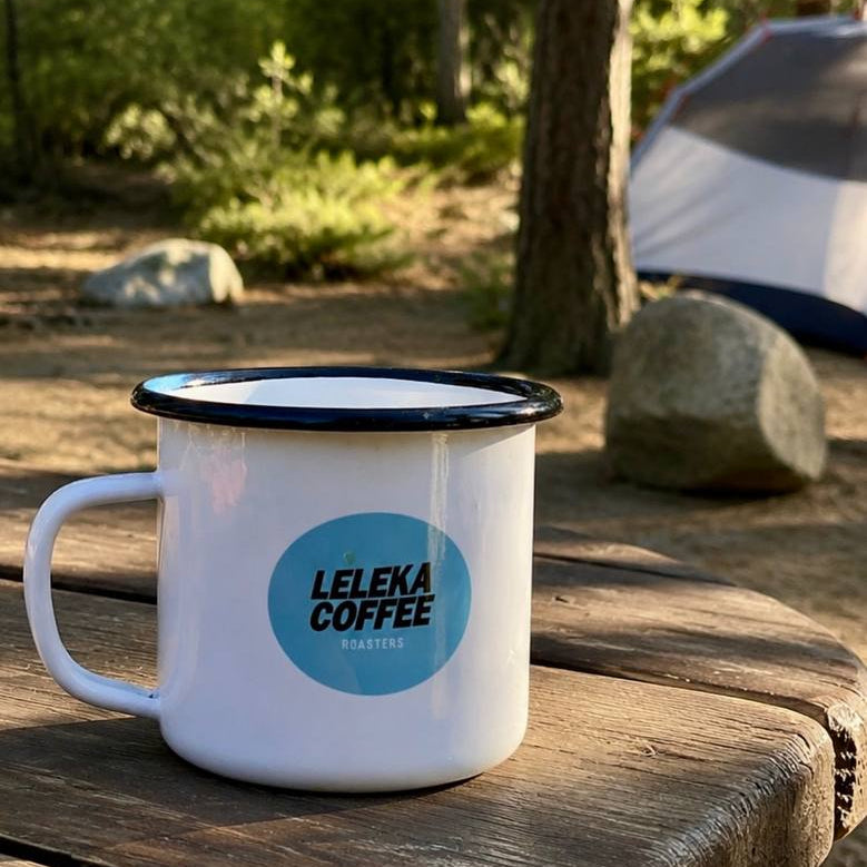 Leleka Coffee mug on a wooden table in a forest setting with a tent in the background
